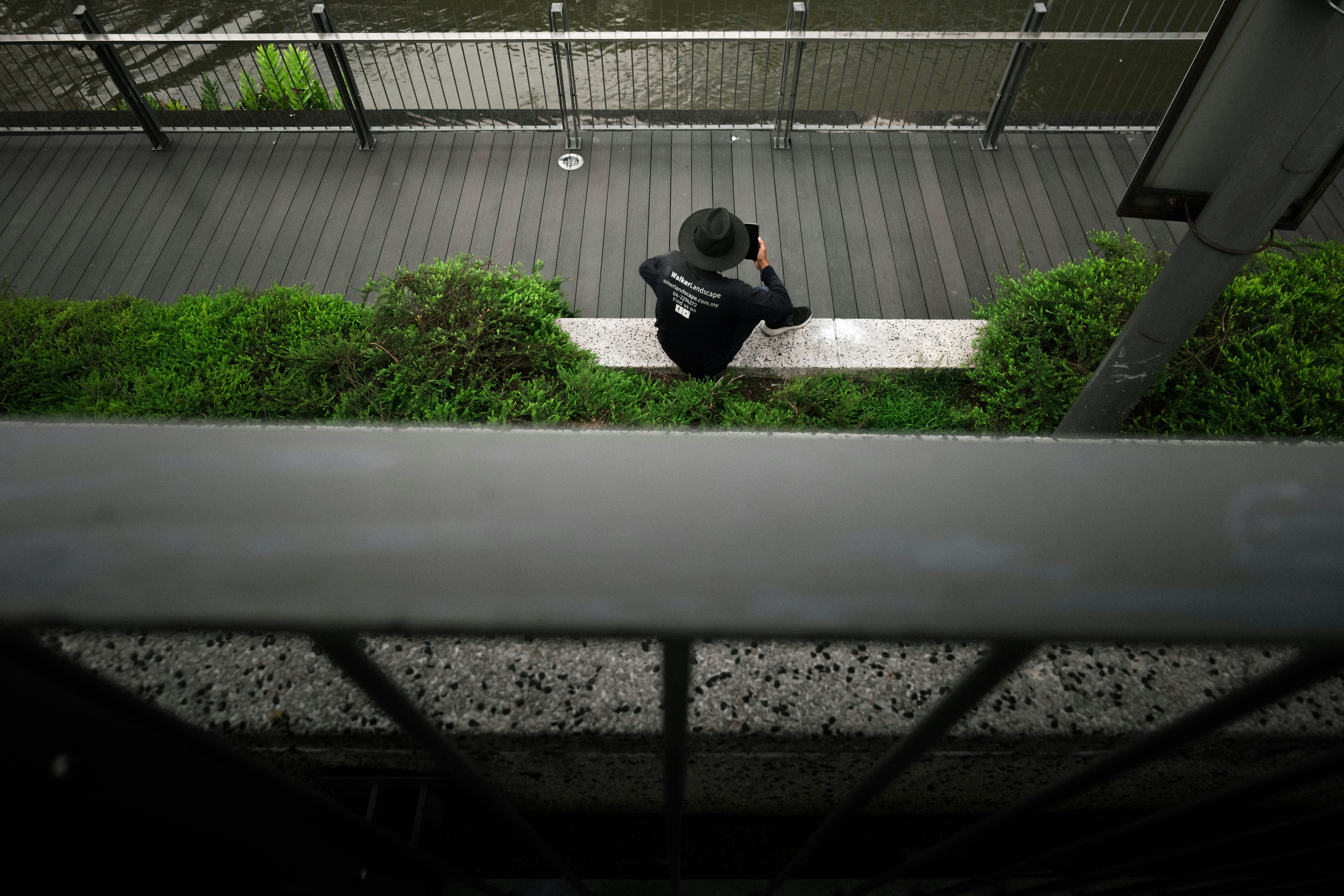 Personne assise sur un rebord avec de l’herbe et une balustrade.