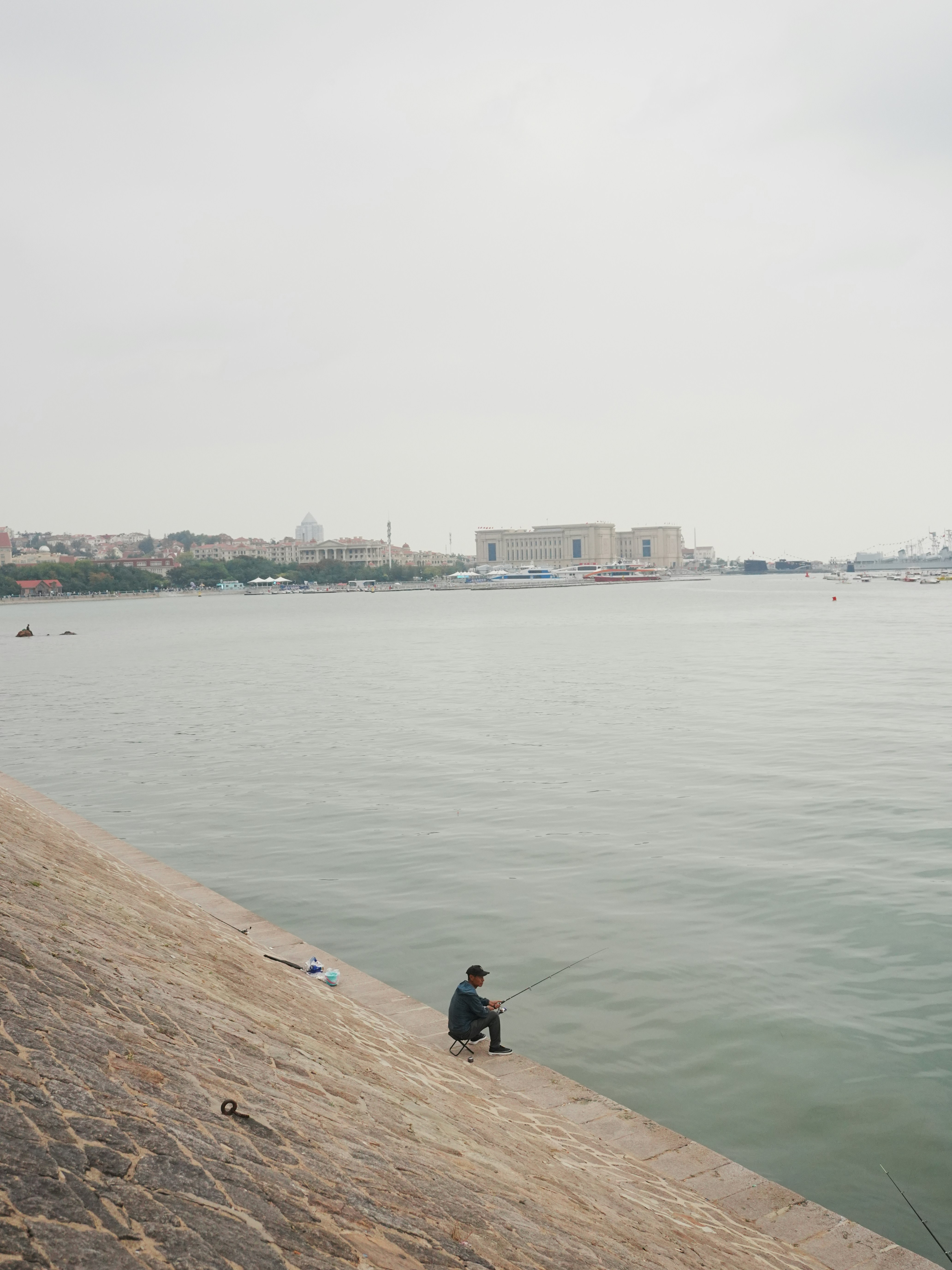 Man fishing on a stone embankment by the water.