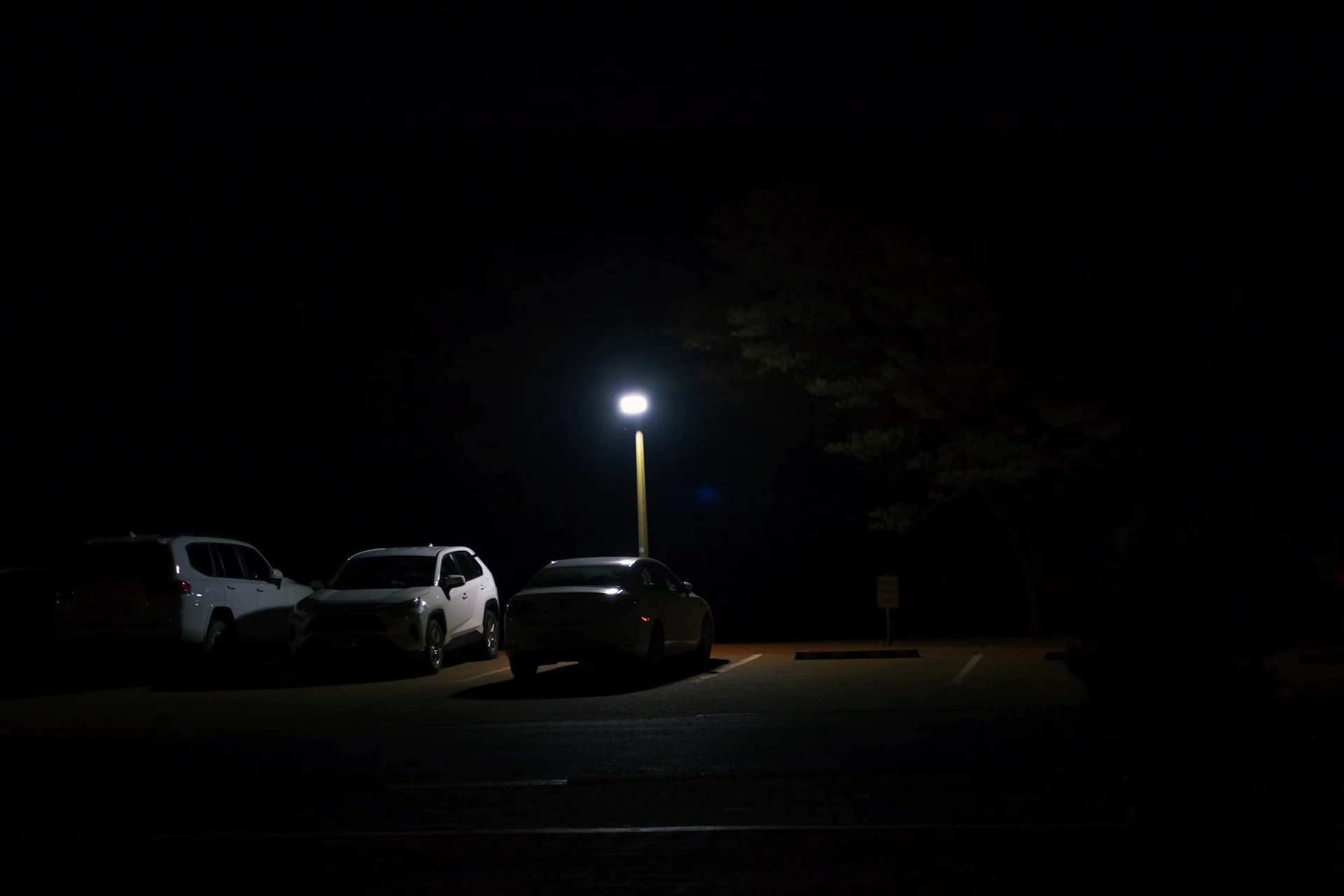 Cars parked in a dark lot under a streetlight.