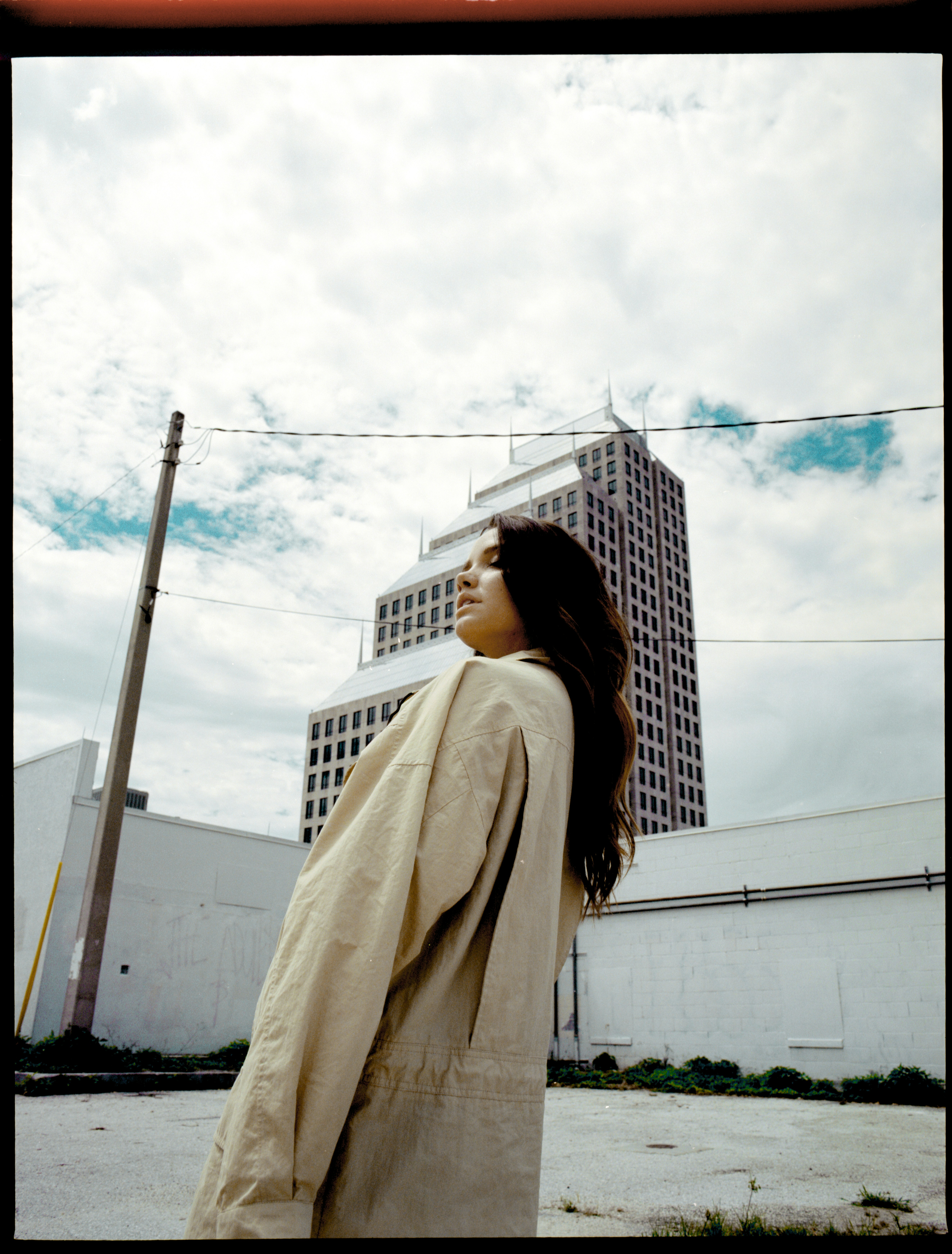 Frau im hellbraunen Mantel steht gegen städtische Gebäude