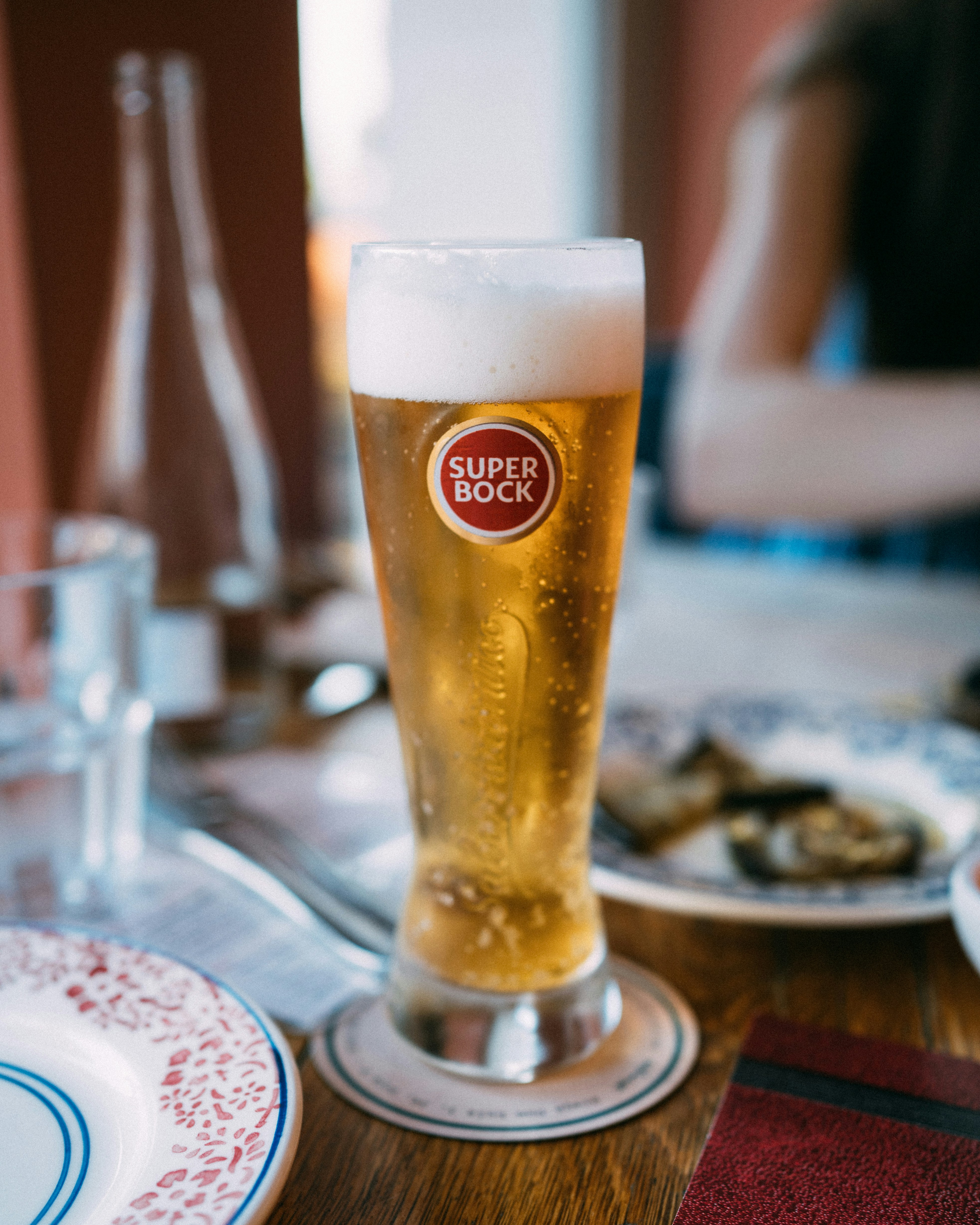 A tall glass of super bock beer with foam.