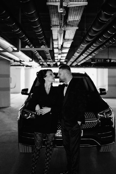 A couple in formal wear stands by a luxury car.