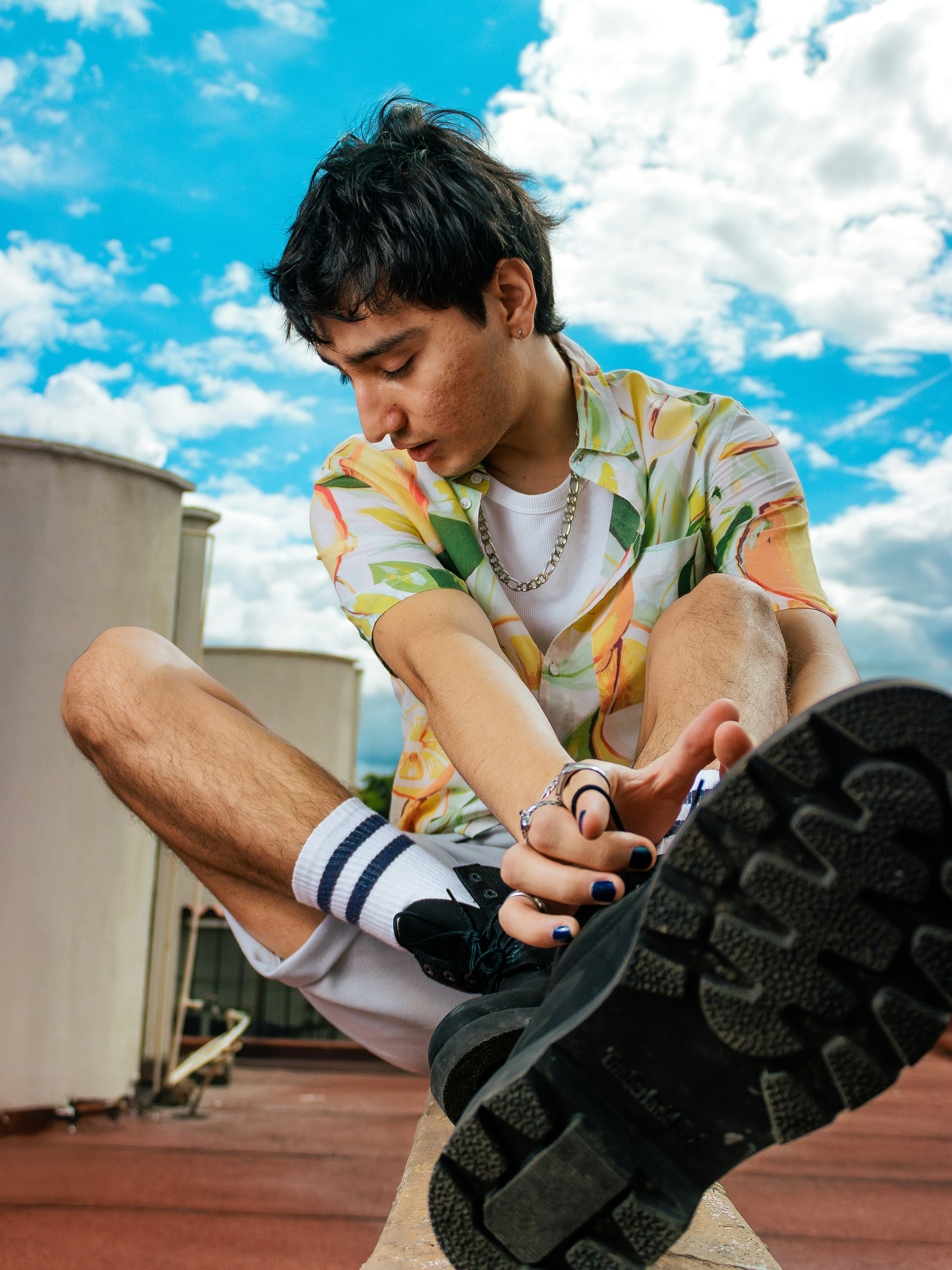 Young man in colorful shirt sits outdoors against sky.
