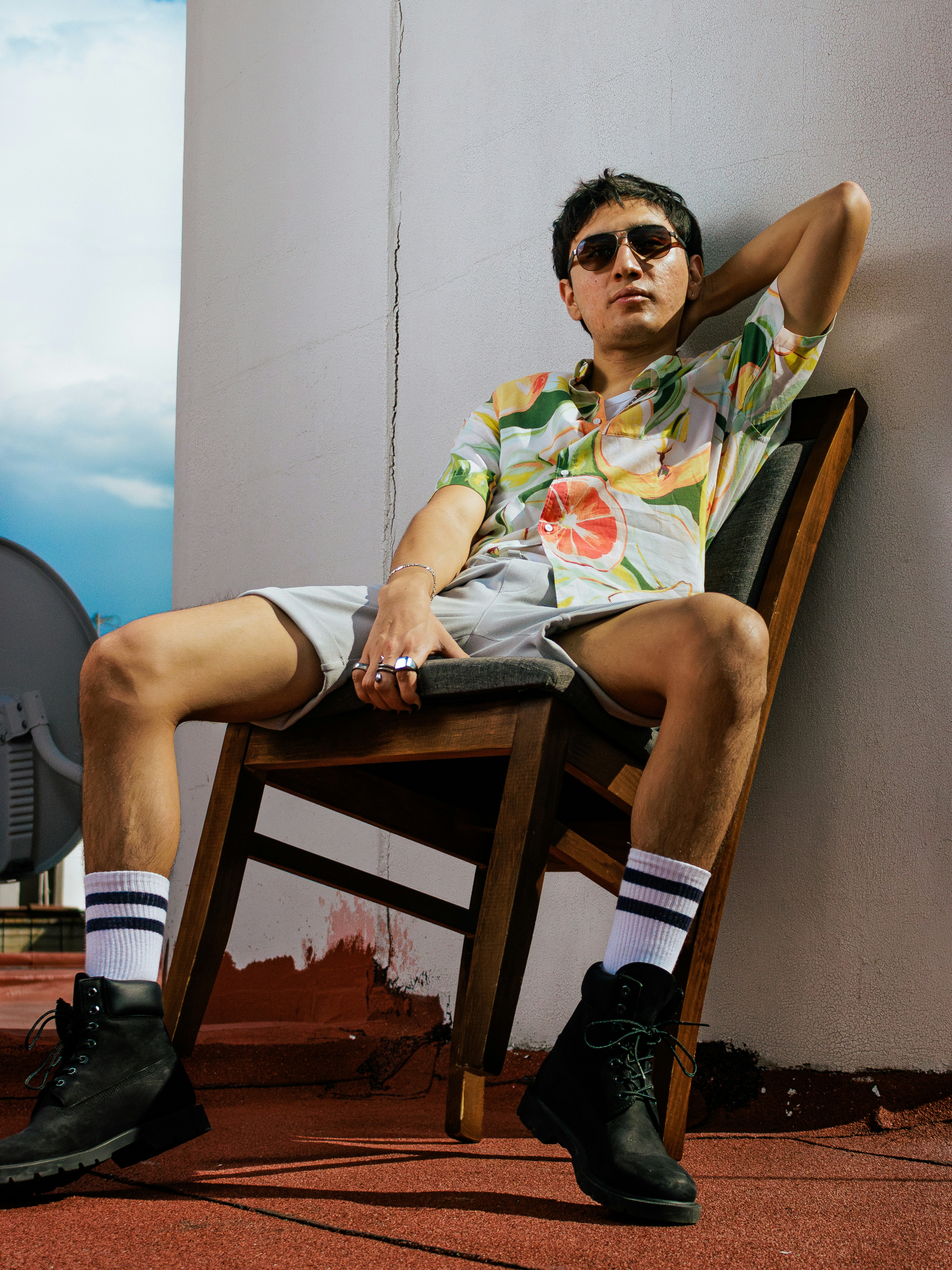Man in hawaiian shirt and shorts sitting on chair.