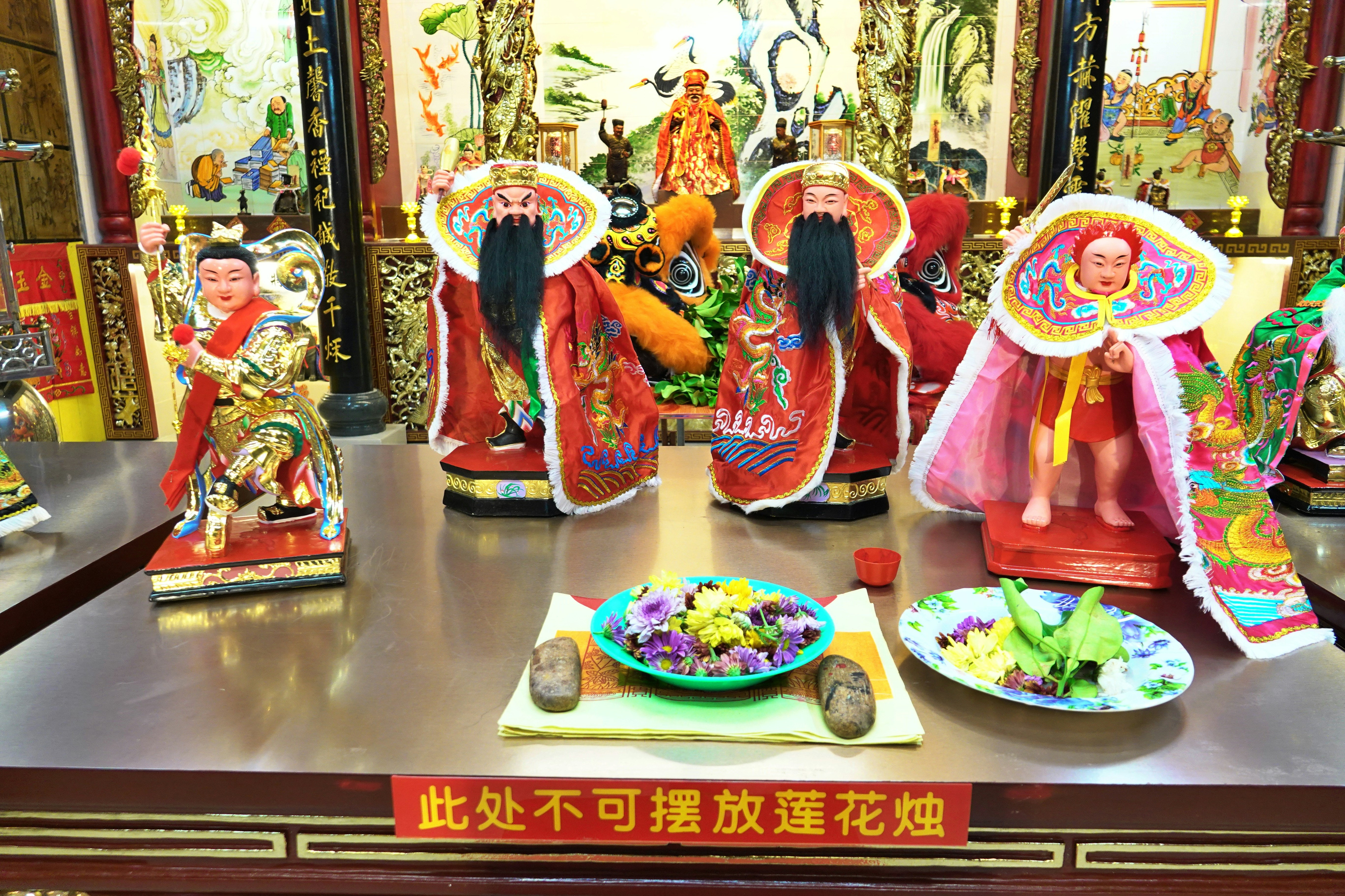Three ornate statues with offerings in a temple.