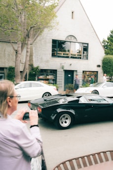 A person photographs a black vintage sports car.