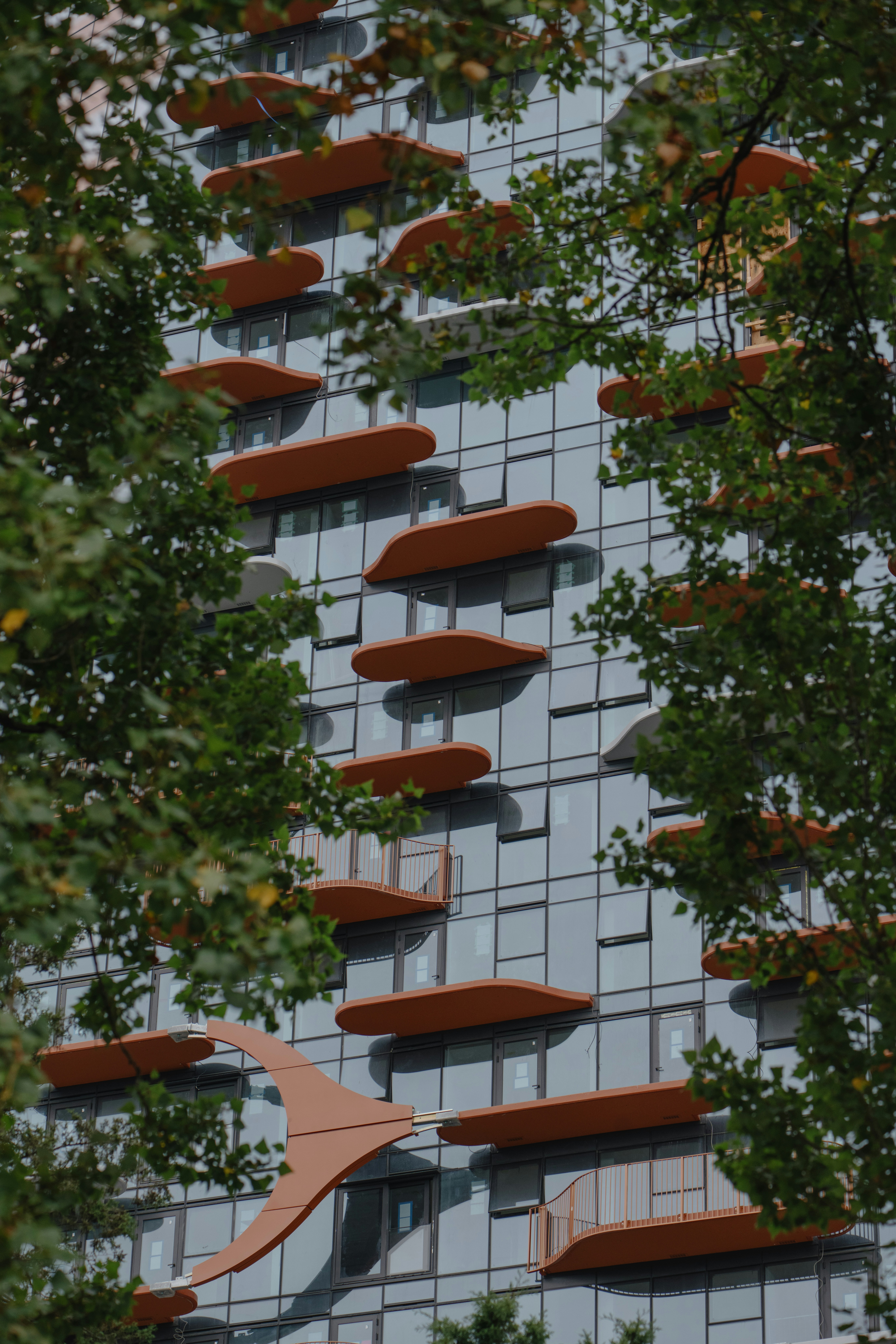 Modern building with unique orange balconies and green trees.