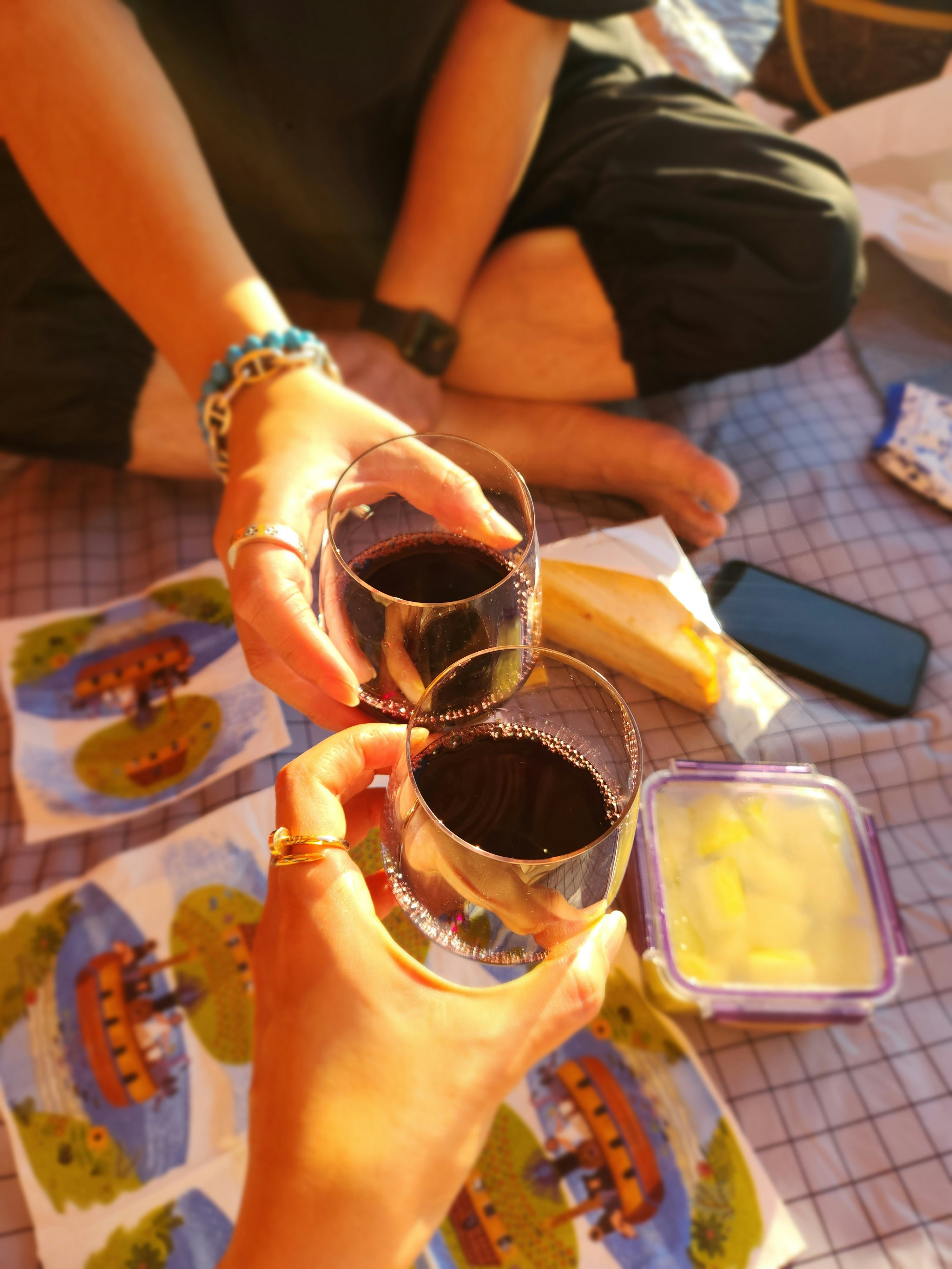 Two hands clinking glasses of red wine during picnic.