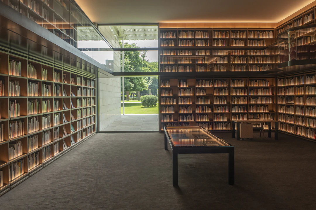 A sunlit contemporary library with floor-to-ceiling wooden bookshelves opening onto a garden