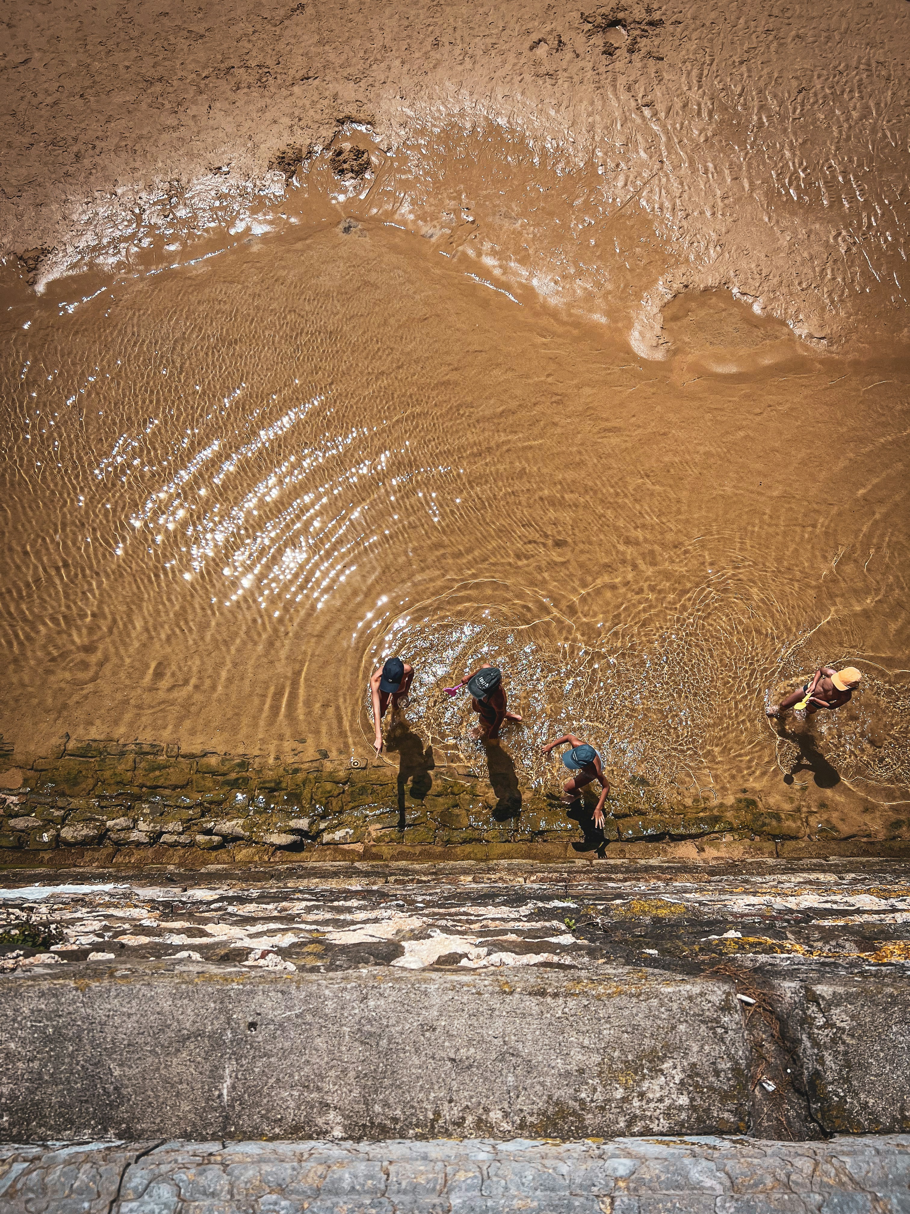 돌담 근처의 얕은 물을 헤쳐나가는 사람들.