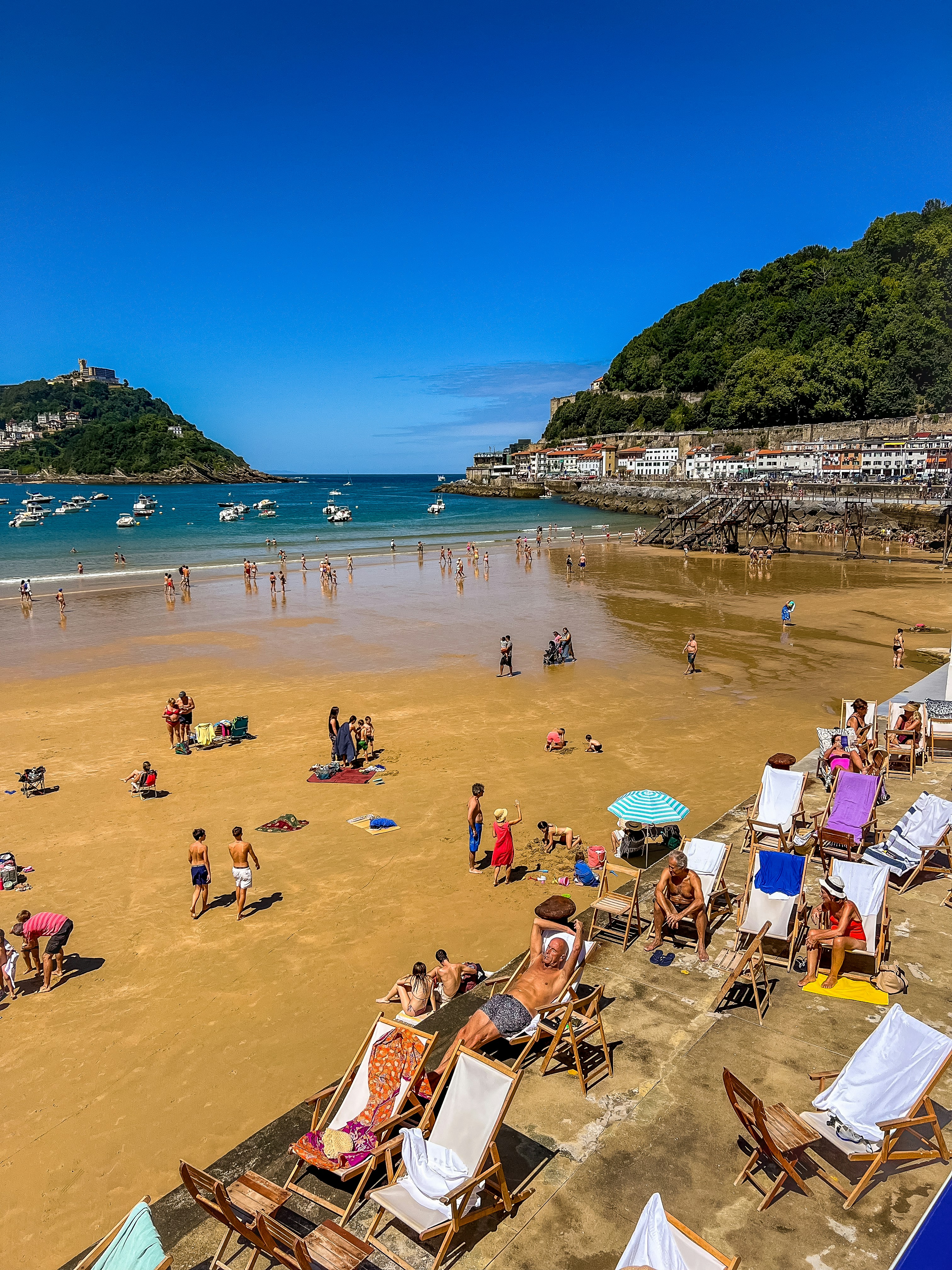 사람들은 붐비는 만이 내려다보이는 해변 의자에서 휴식을 취합니다.