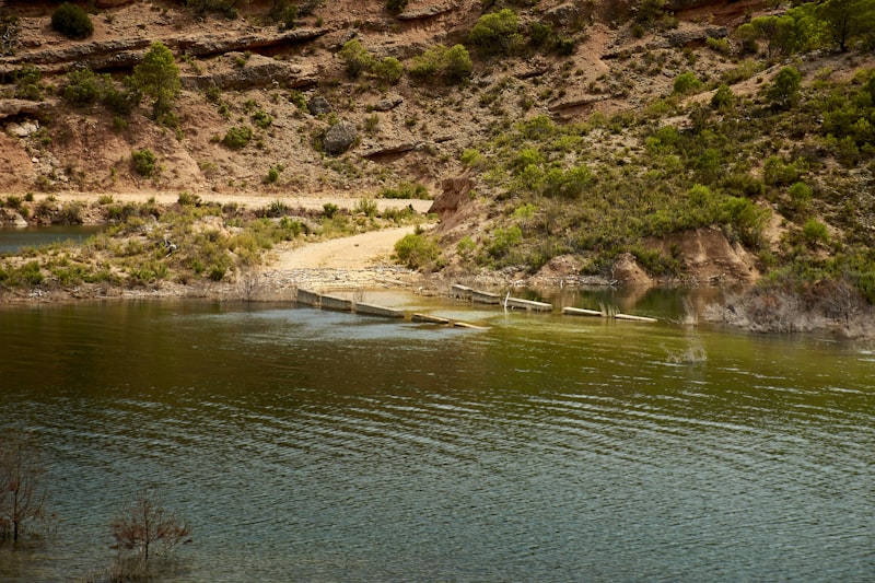 A wooden bridge crosses a calm lake surrounded by hills.