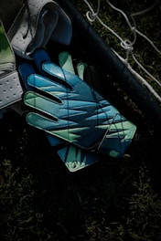 Goalkeeper gloves resting on grass near a net.