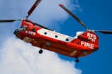 Red and white firefighting helicopter flying in blue sky.