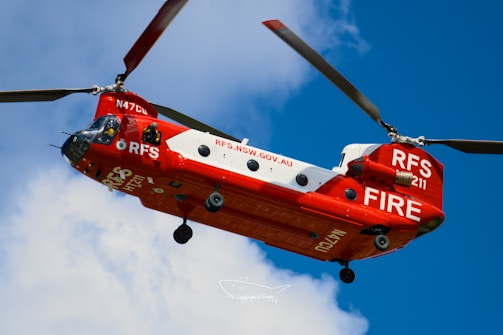 Red and white firefighting helicopter flying in blue sky.