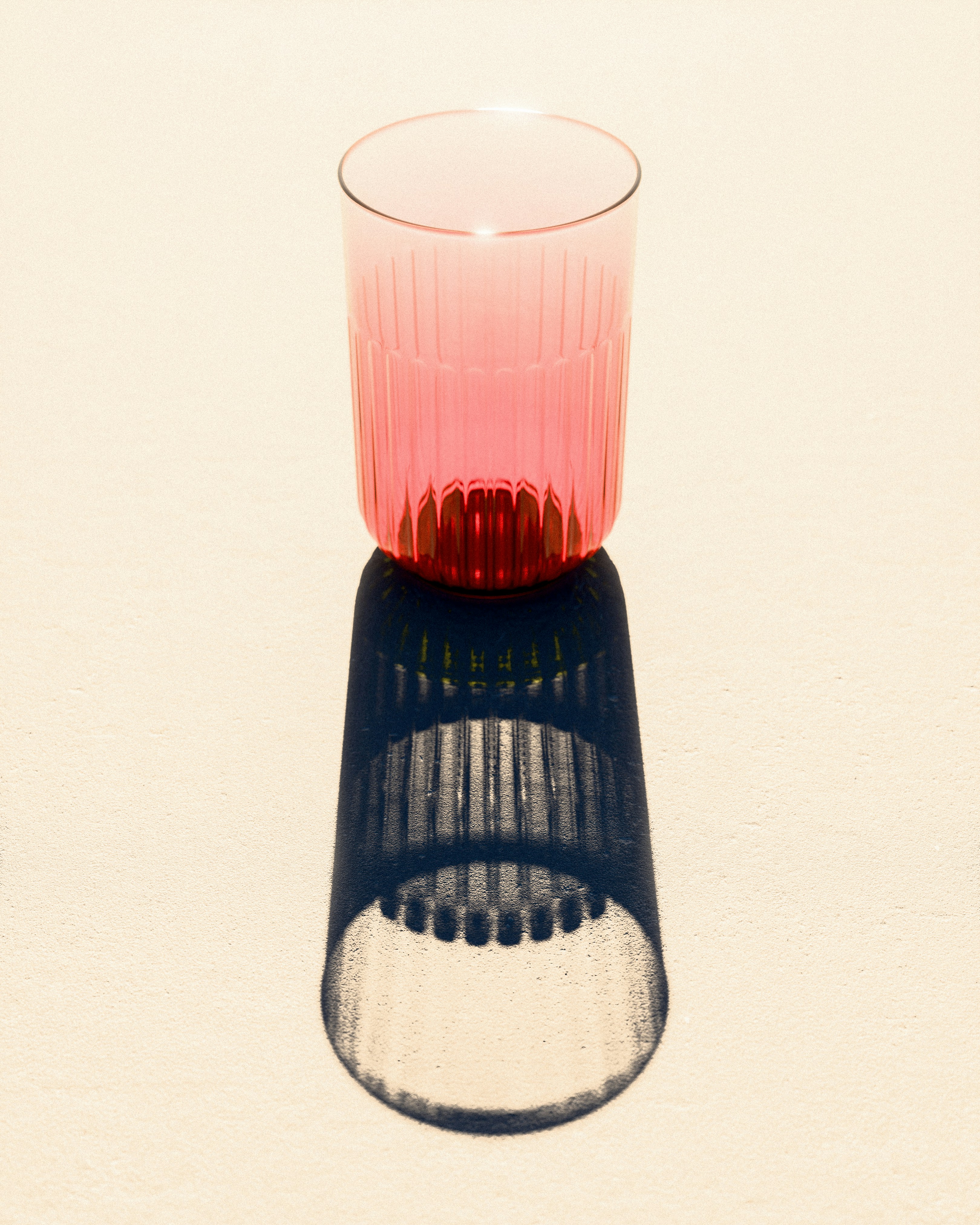 A pink glass casting a shadow on a white surface