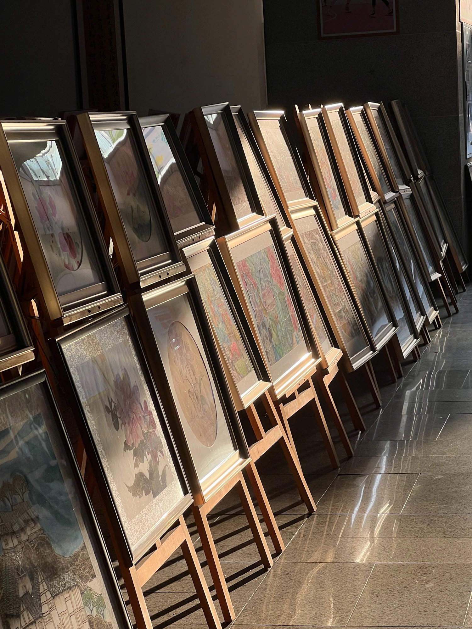Framed works standing on easels in a row before being hung