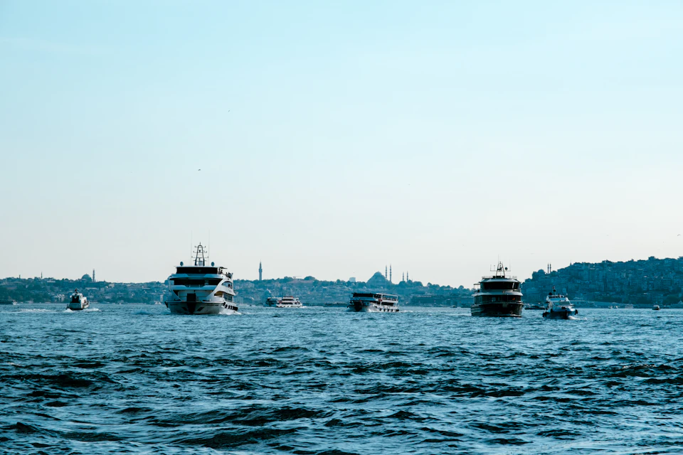 Multiple boats sail through calm Bosphorus waters with vibrant contrasting colors nearby