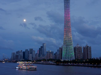 Modern cityscape with illuminated tower and boat at dusk