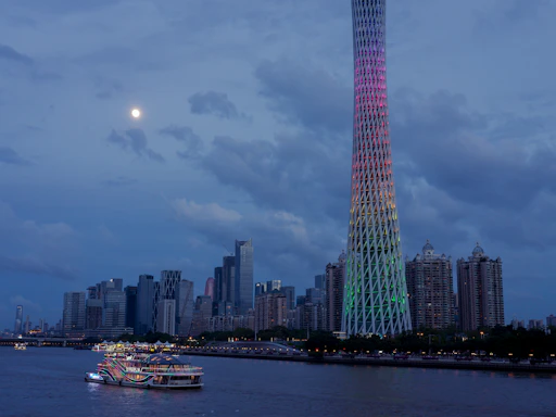 Modern cityscape with illuminated tower and boat at dusk