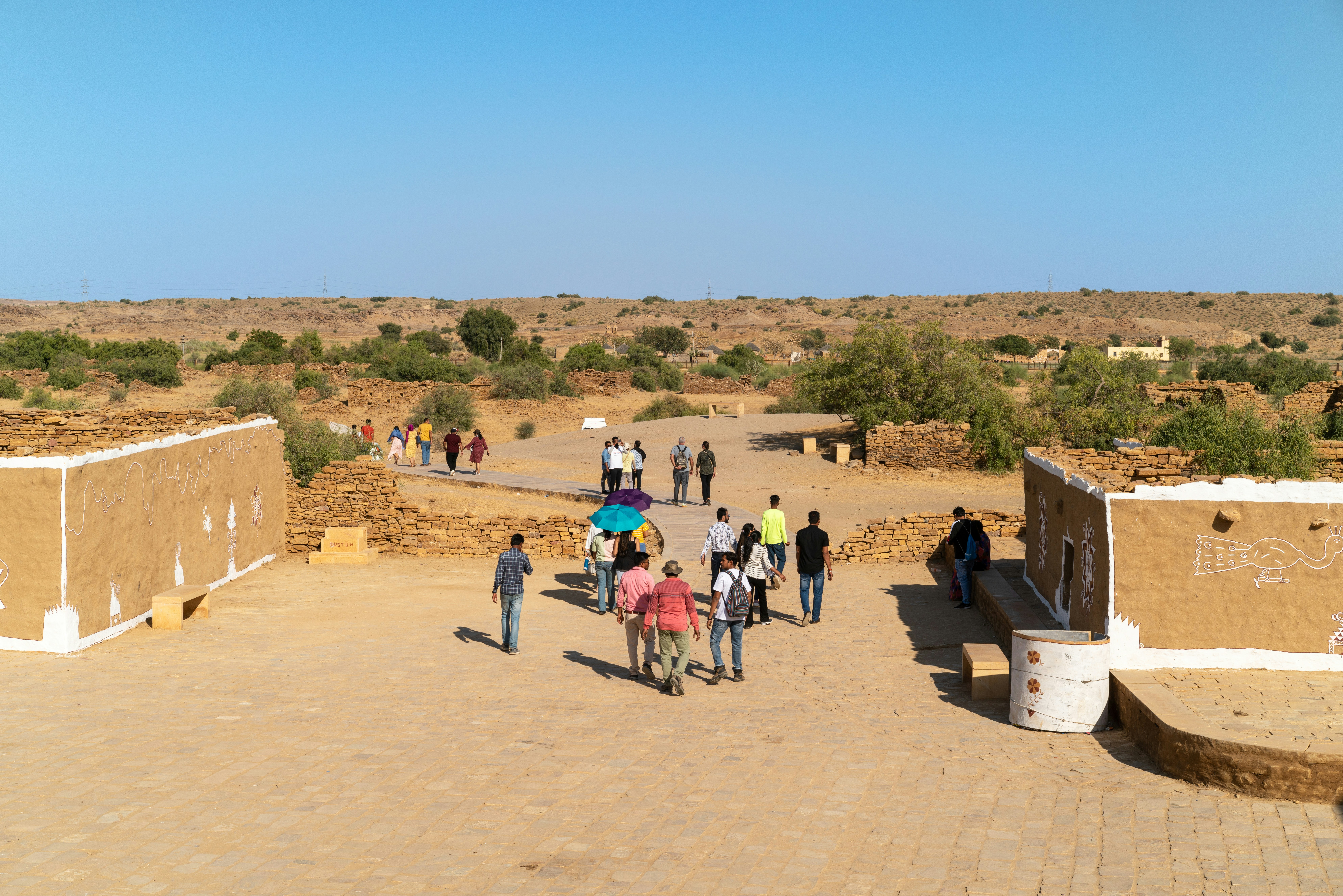 People walking through a desert village on a sunny day.