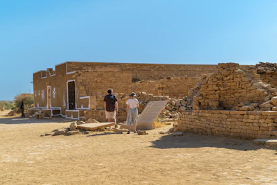 Two people walk through ancient ruins under a clear sky.