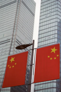 Two chinese flags on a pole with skyscrapers behind.