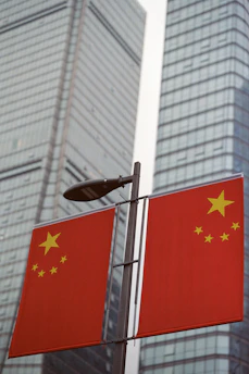 Two chinese flags on a pole with skyscrapers behind.