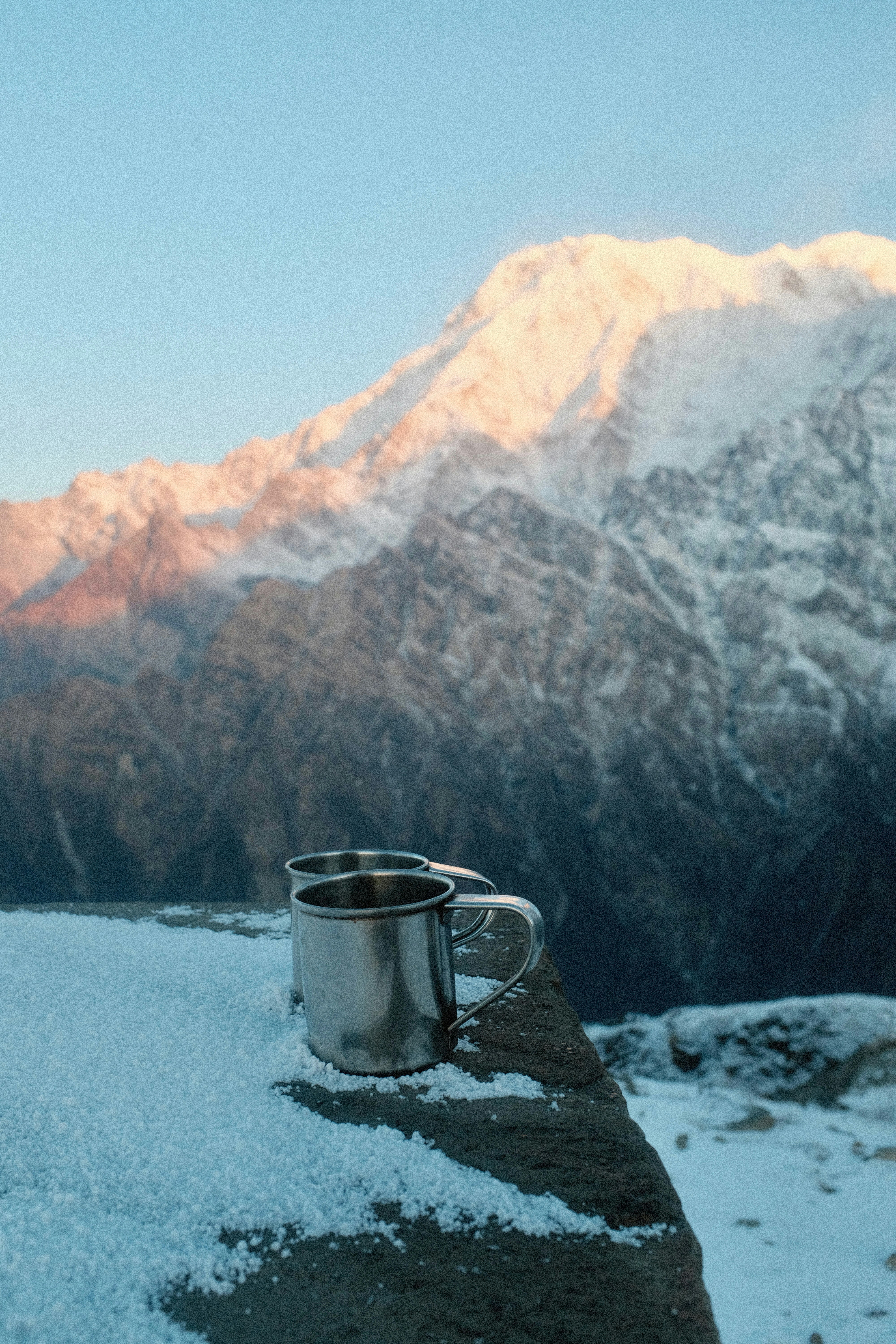 Zwei Metallbecher auf verschneitem Felsvorsprung mit Bergkulisse