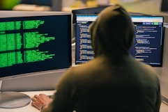 Hacker in hoodie working on multiple computer screens