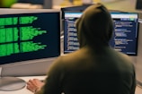 Hacker in hoodie working on multiple computer screens