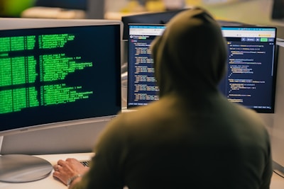 Hacker in hoodie working on multiple computer screens