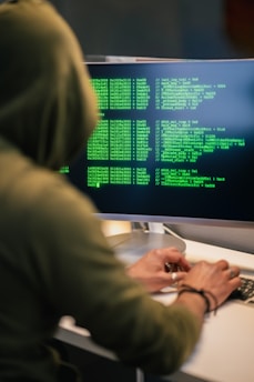 Person in hoodie typing code on computer screen.