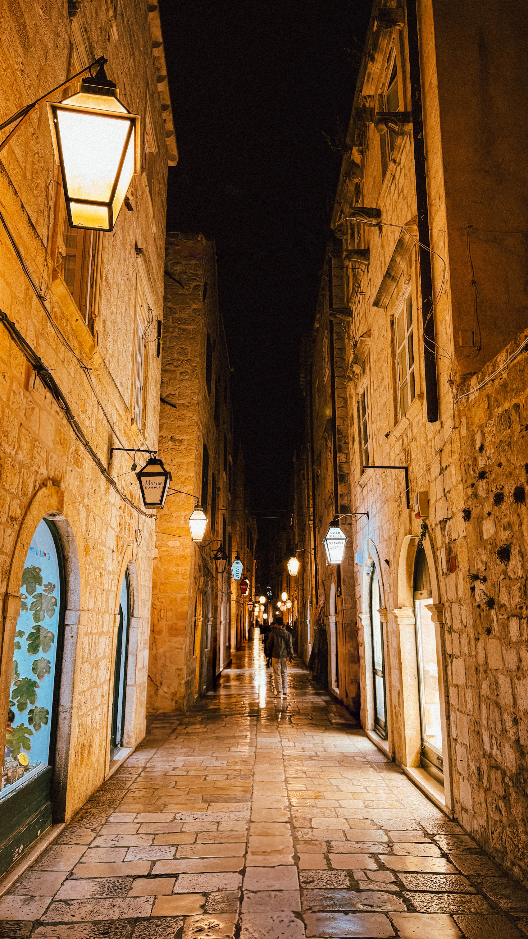 A warmly lit limestone lane in Dubrovnik's old city after rain at night