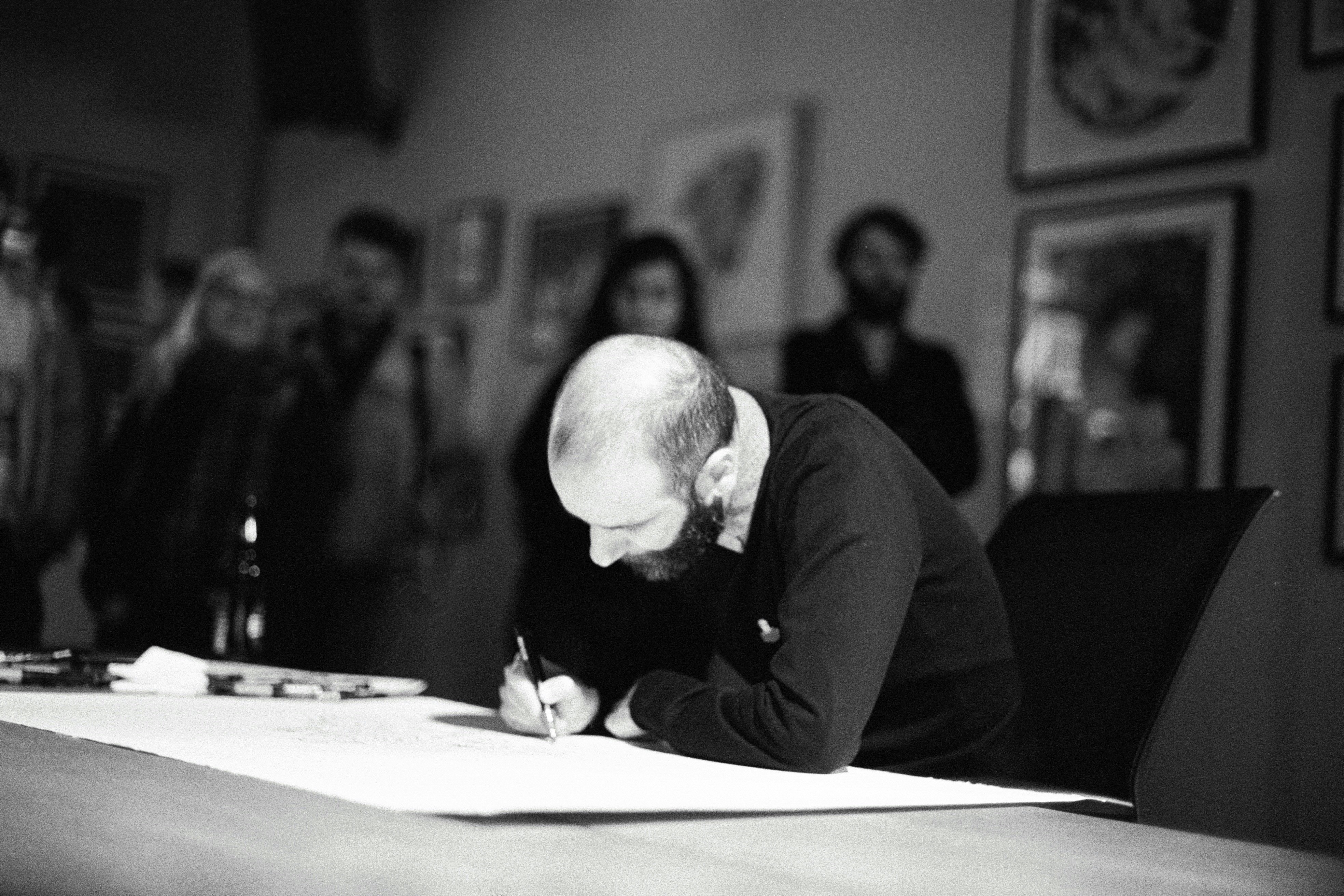 Man signing a document at a table with people watching.