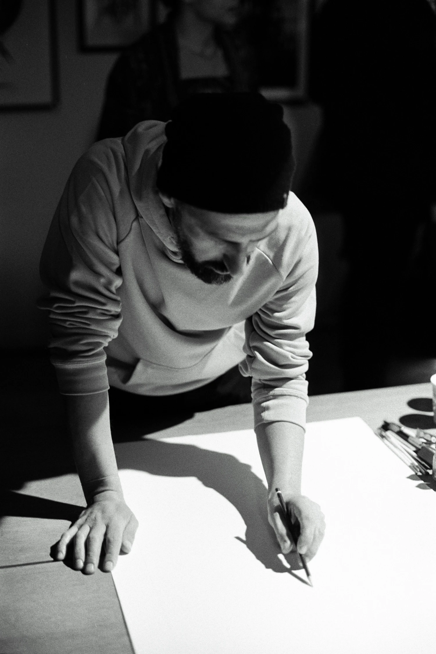 Black and white photo of an artist leaning over a large sheet, drawing with a pencil