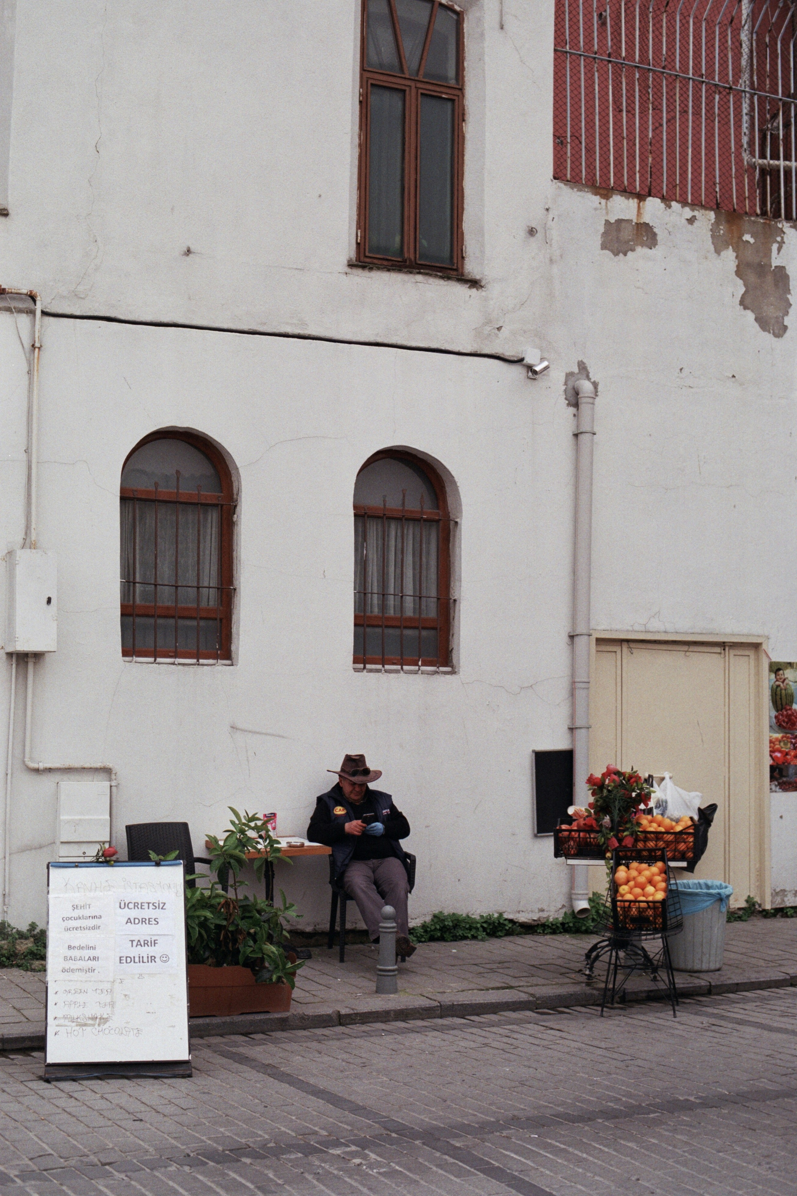 Man sitting outside building near fruit stand
