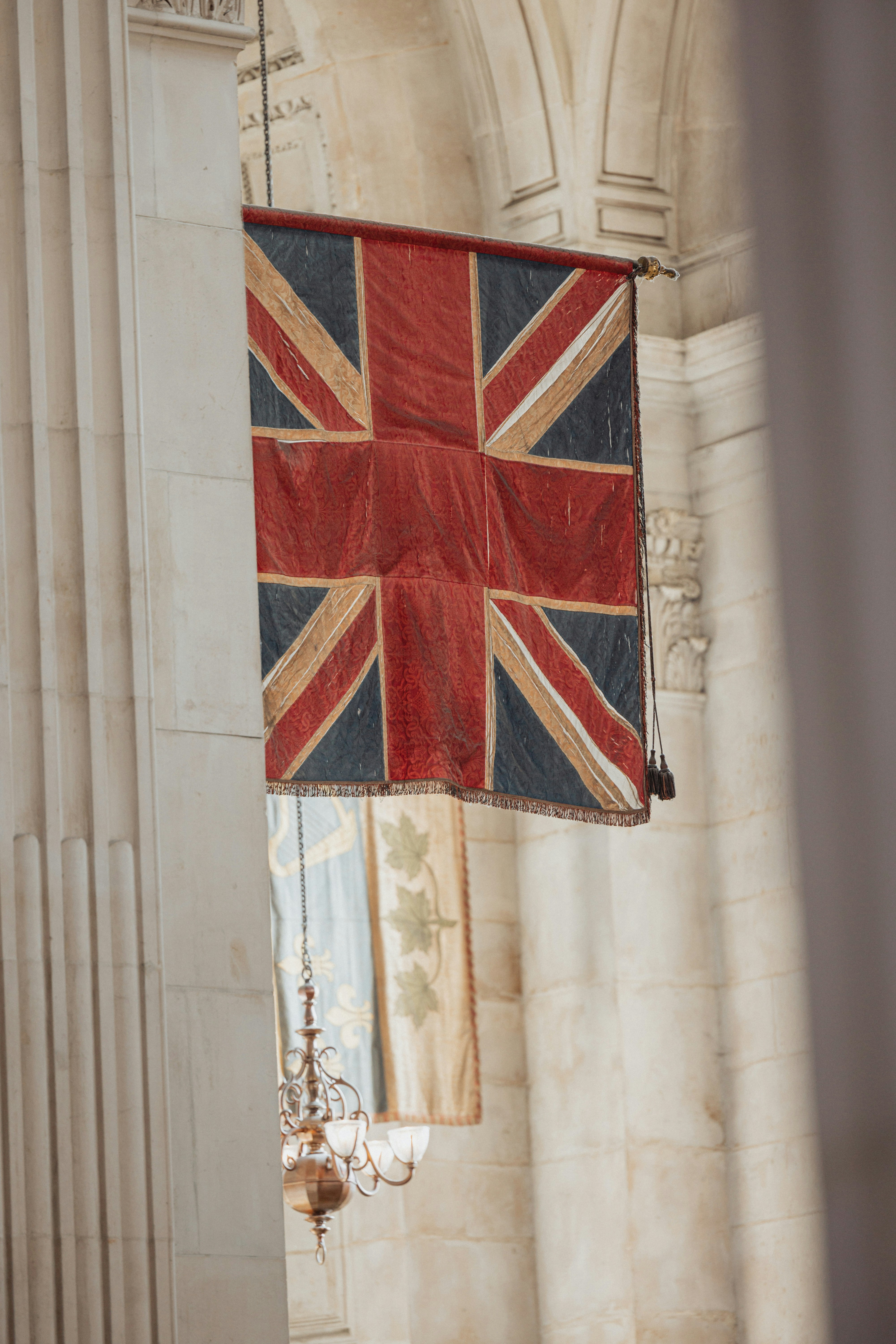 Union jack flag hanging indoors with ornate chandelier.