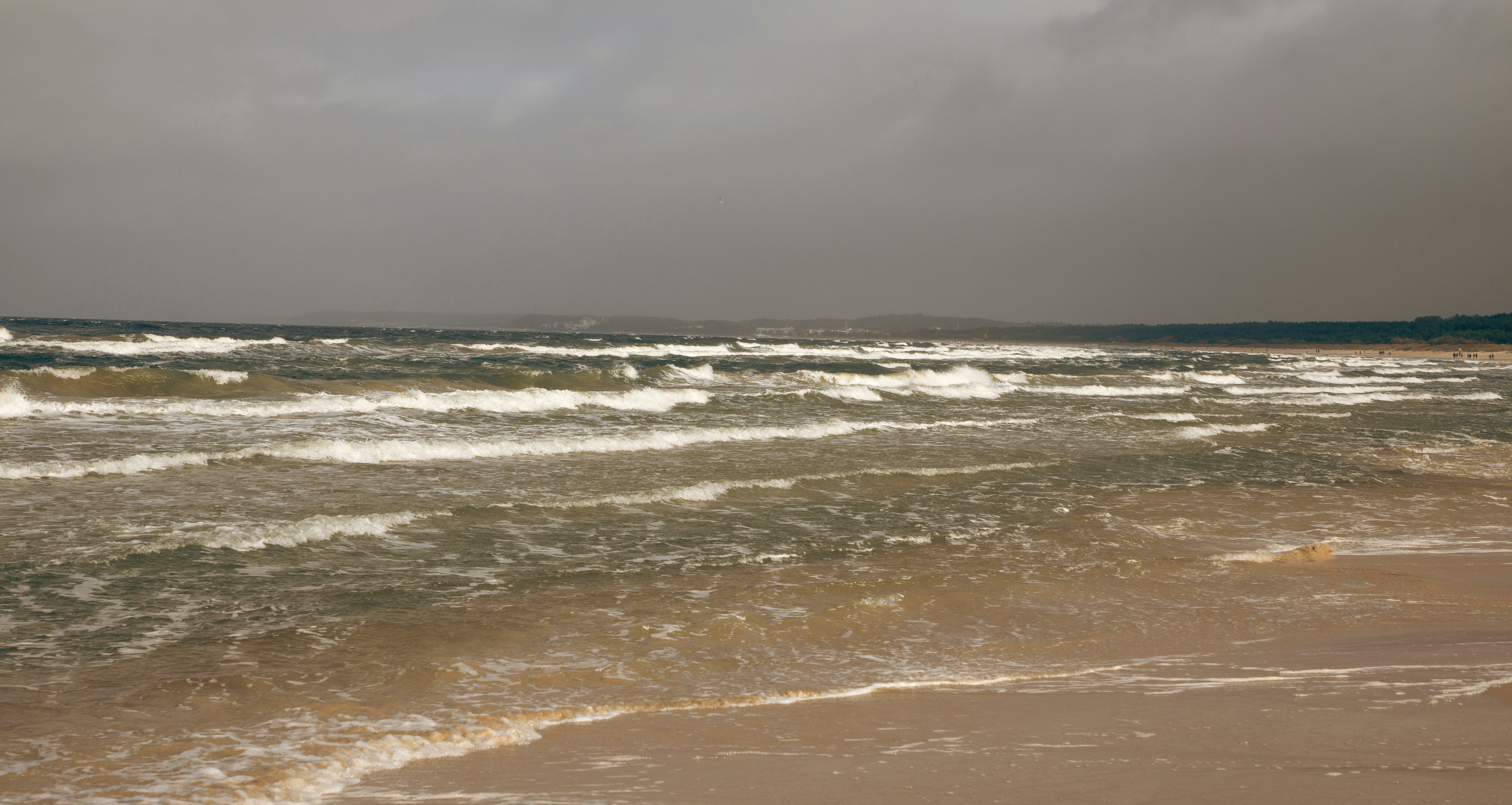 Rough waves crash on a sandy beach under stormy skies.