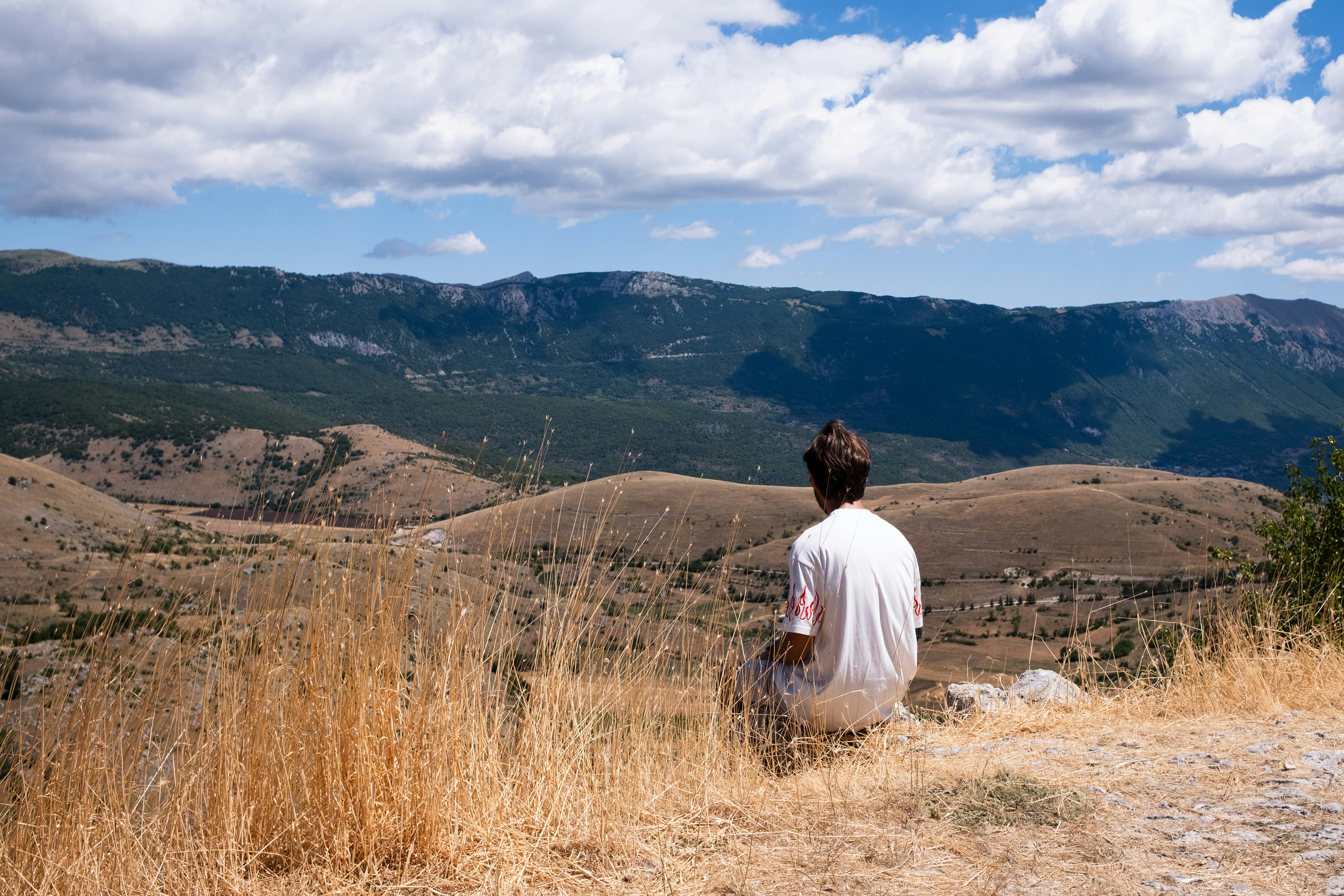 A person sits looking at a vast mountain landscape.