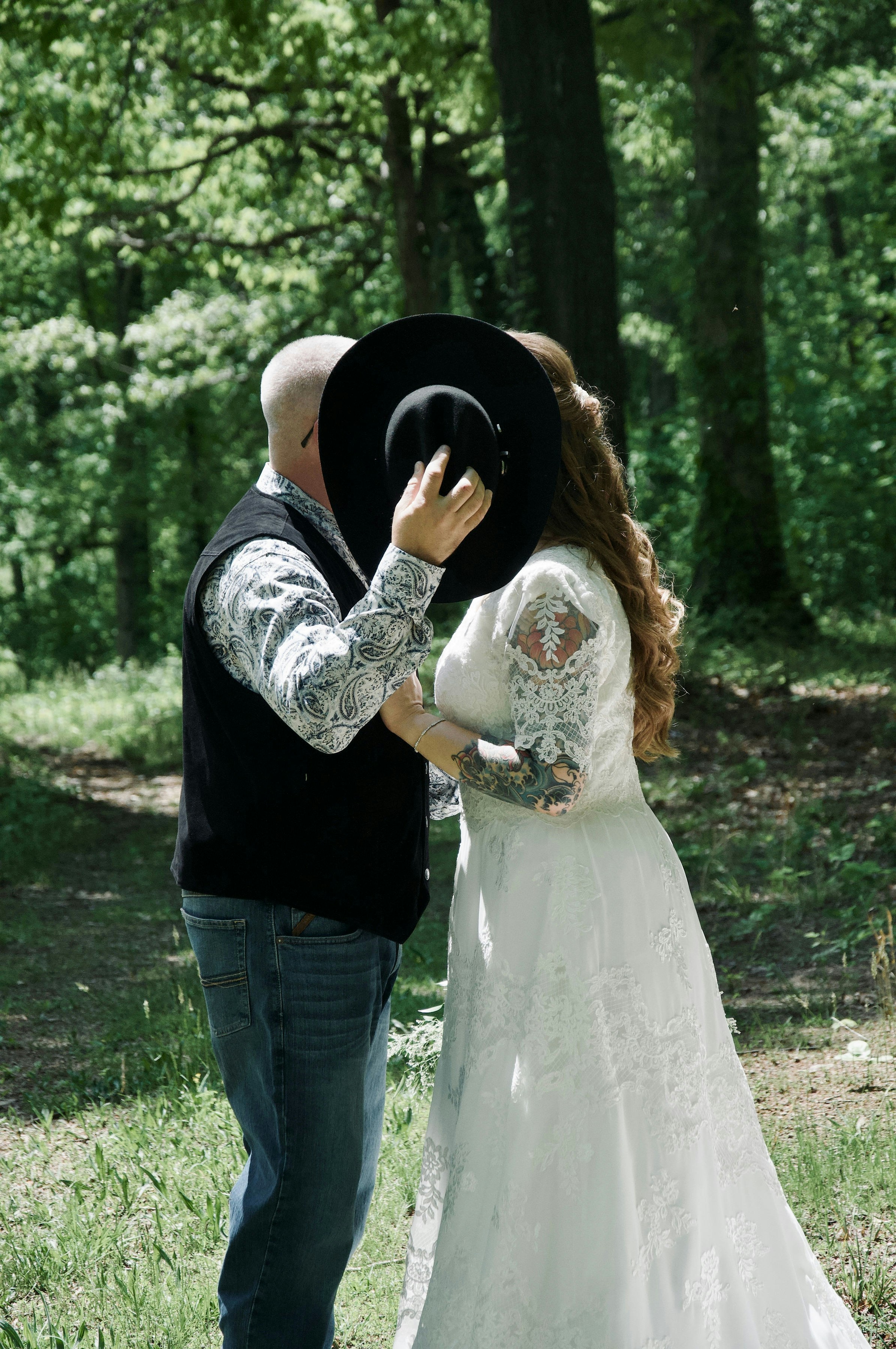 Couple kissing behind a hat in a forest.