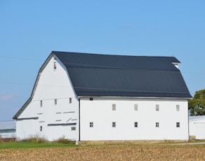 A white barn with a dark roof under blue sky