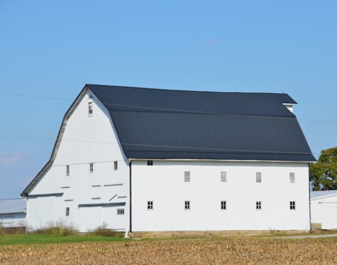 A white barn with a dark roof under blue sky