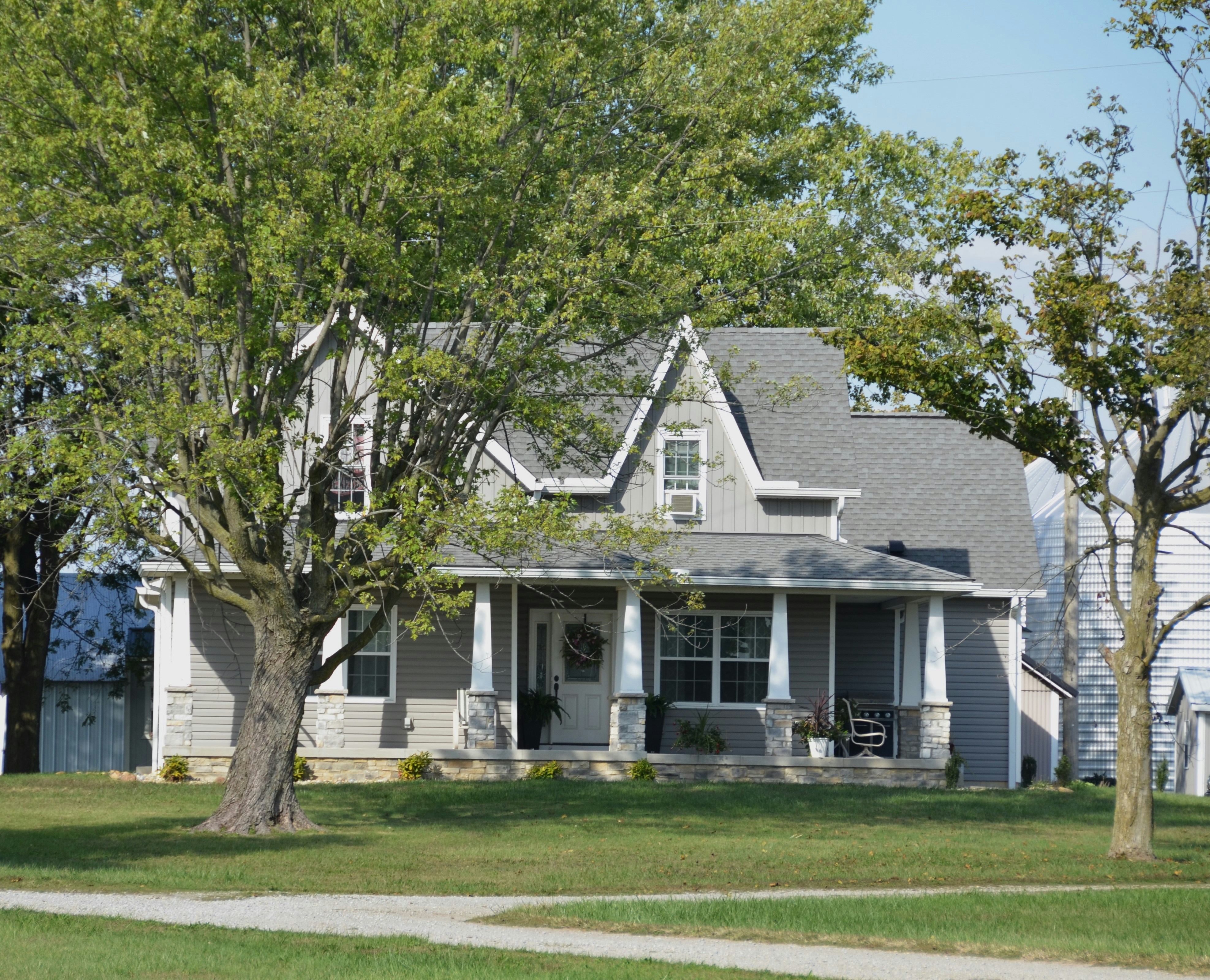A grey house with a porch and trees