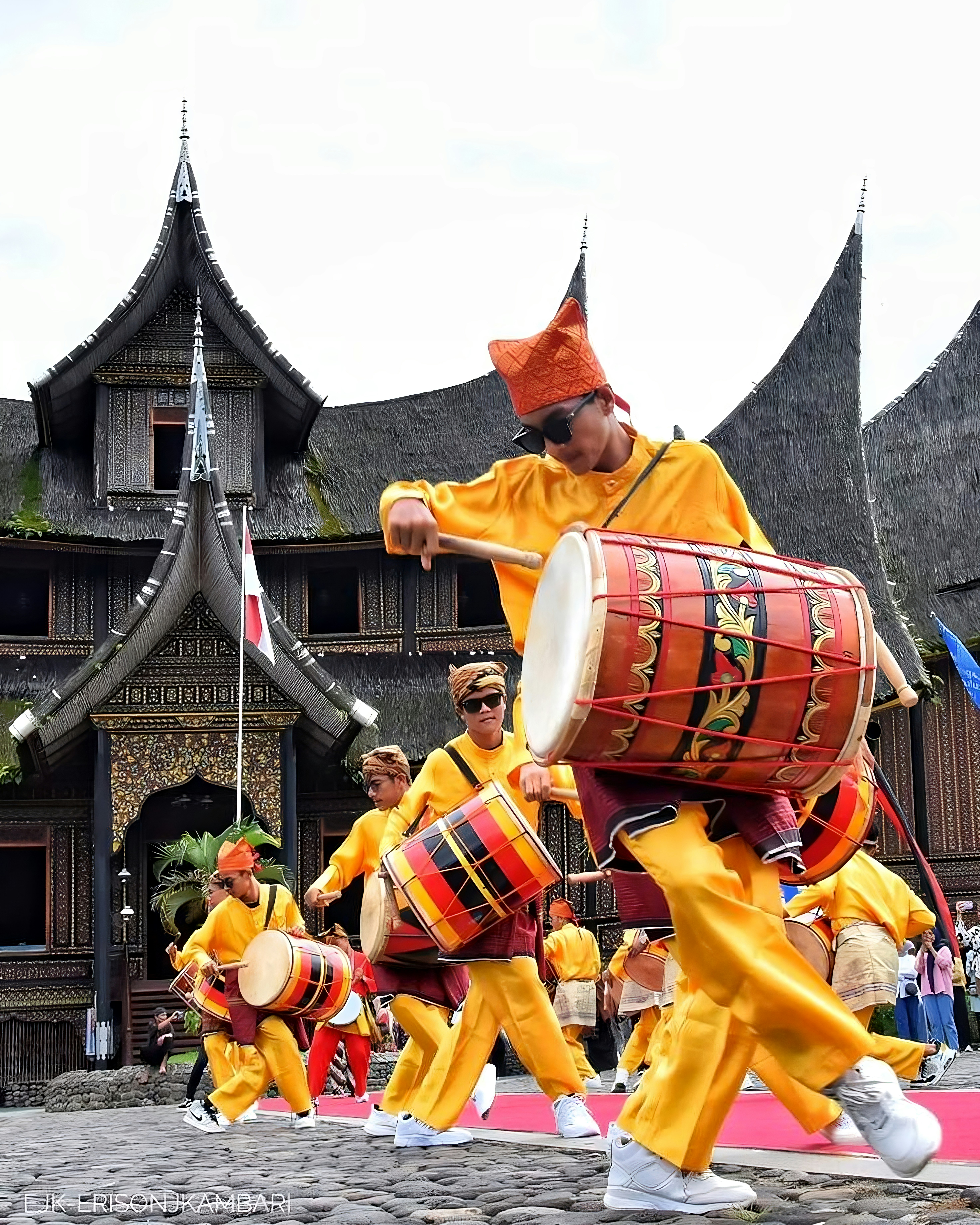 Men in yellow playing drums in front of traditional building
