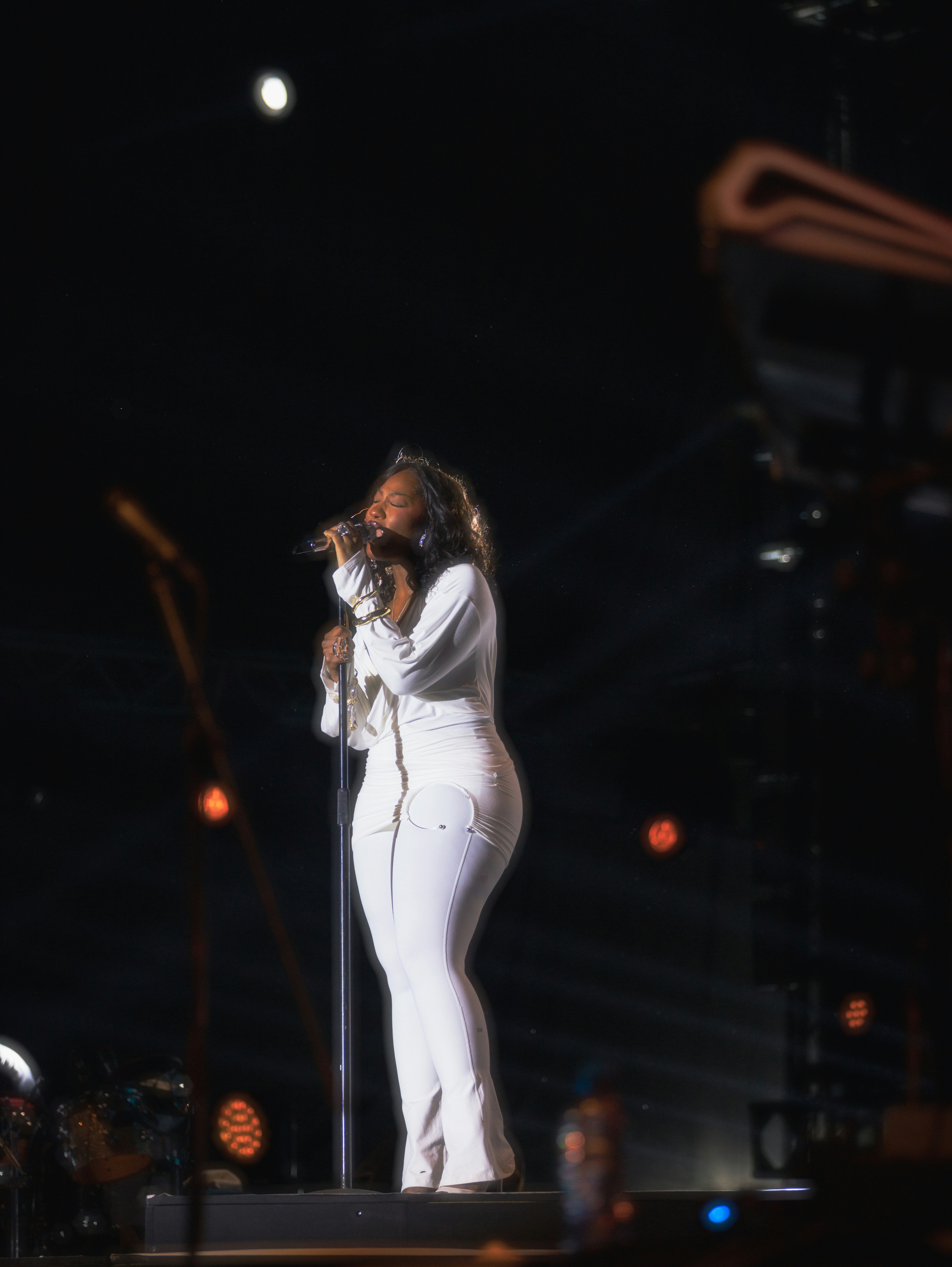 A woman in white sings into a microphone on stage.