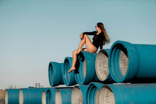 Woman in black bodysuit sitting on large blue pipes