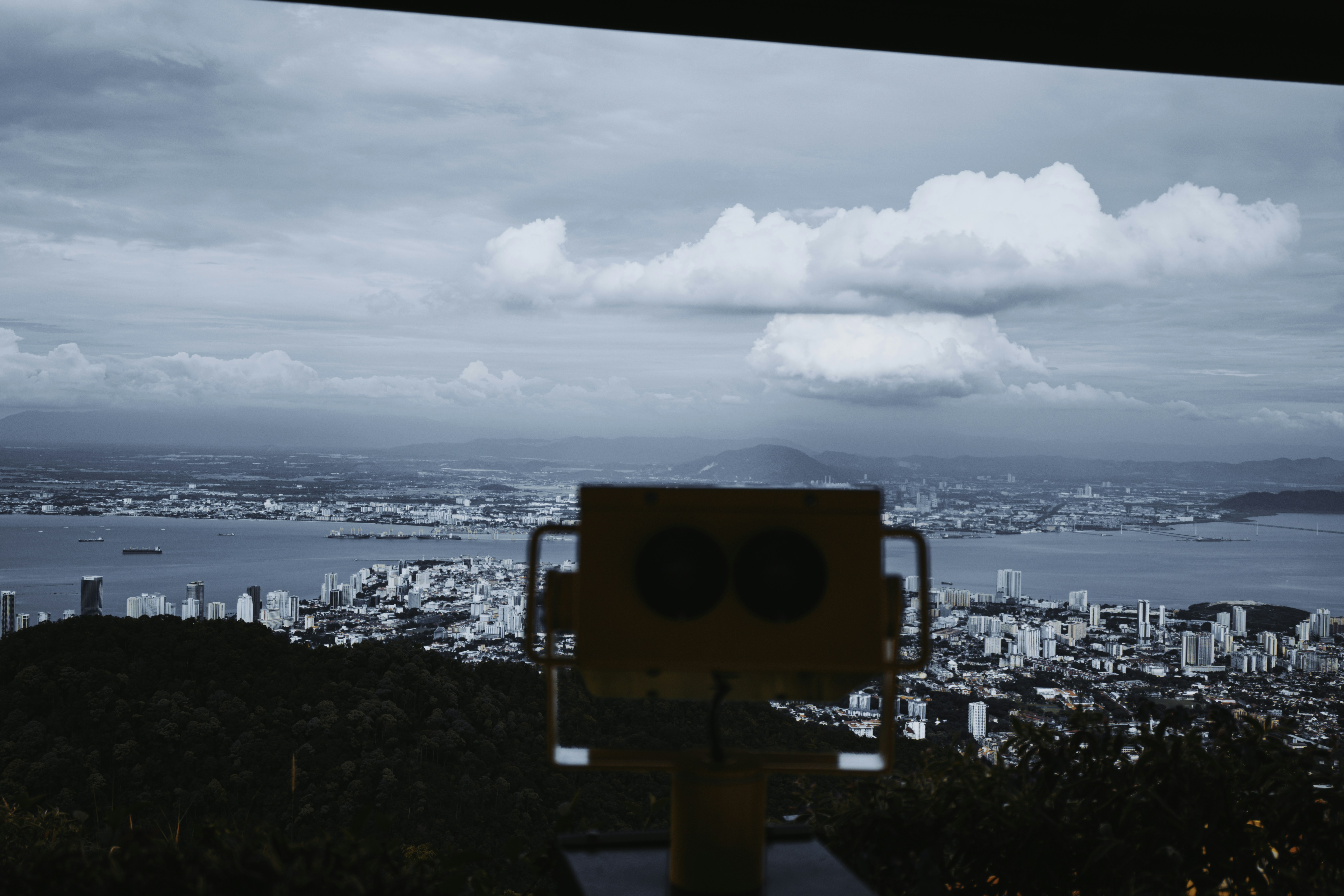 Binoculars overlook a coastal city under cloudy skies.