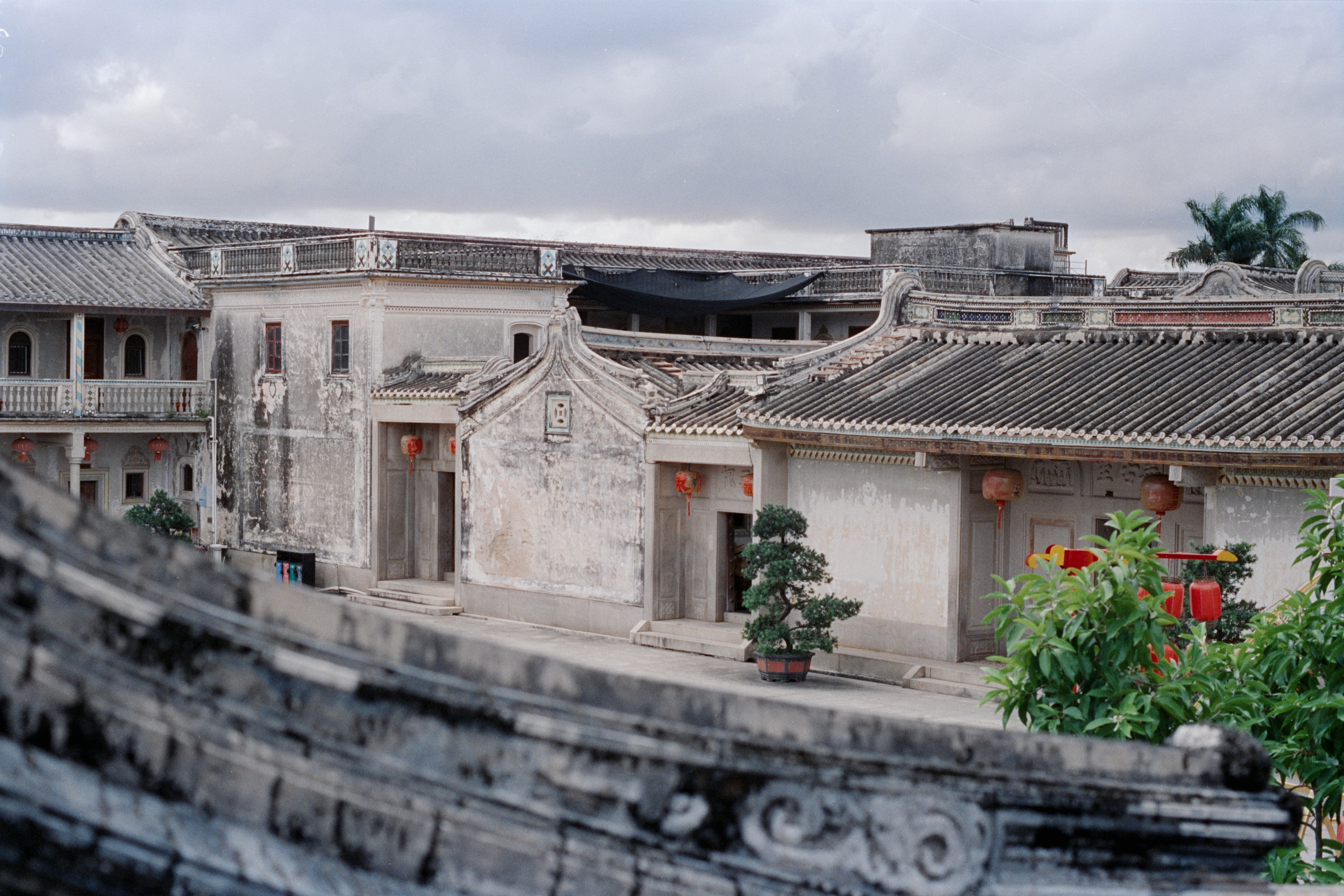 Traditional Chinese courtyard buildings at the Cihong Former Residence in Shantou, China, featuring ancient stone architecture, tiled roofs, red lanterns, and a small potted tree in the courtyard. 