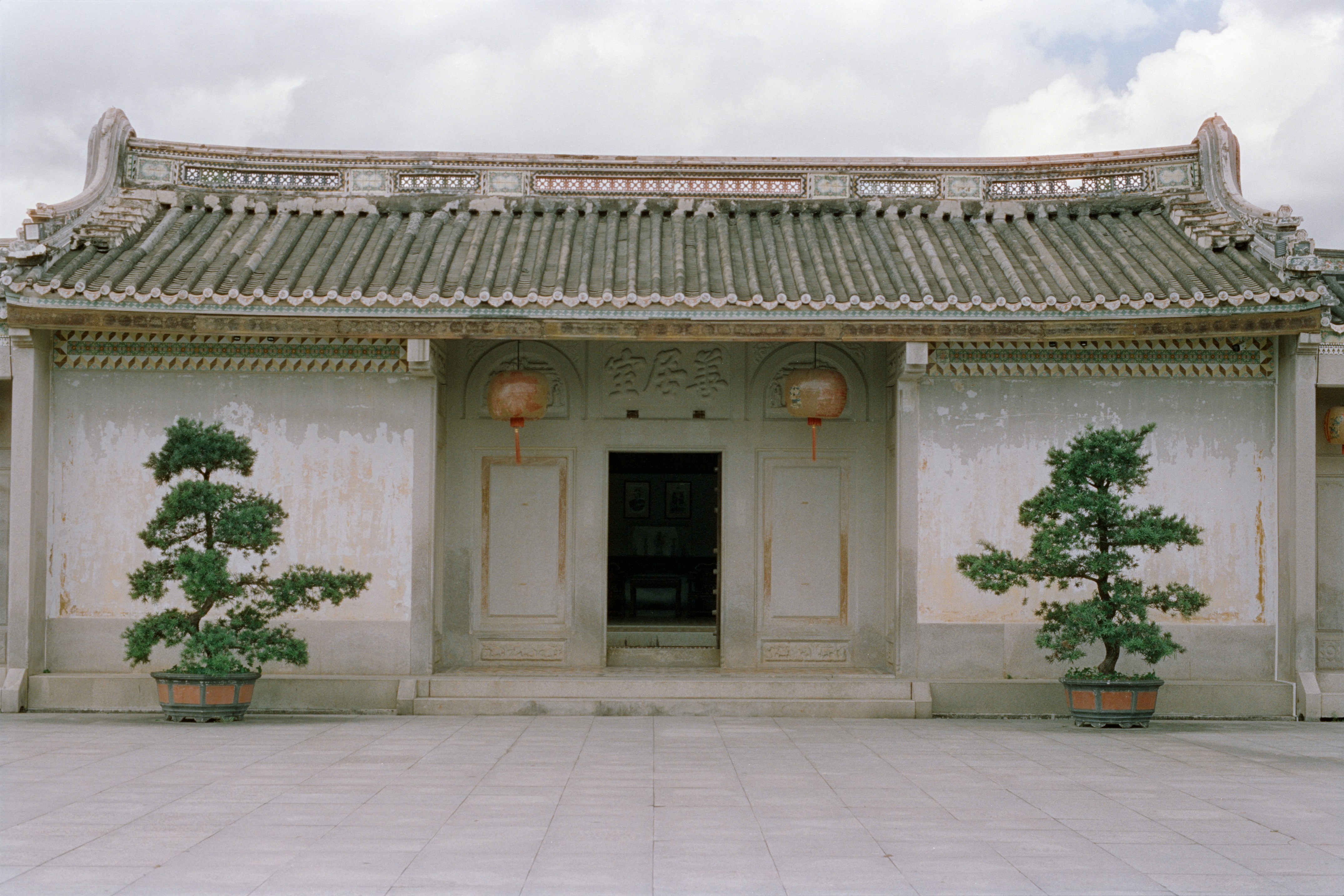 Entrance to the Chen Cihong Former Residence, a traditional Chinese courtyard building with red lanterns and two large potted bonsai trees.